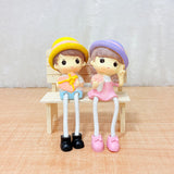 TM0024 Cute Couple Dolls Sitting on Bench with Dangling Legs - Resin Showpiece for Home Decor & Gifting