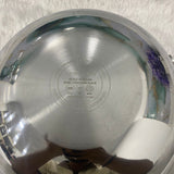 Metallic pressure cooker lid with brand name on a textured white background